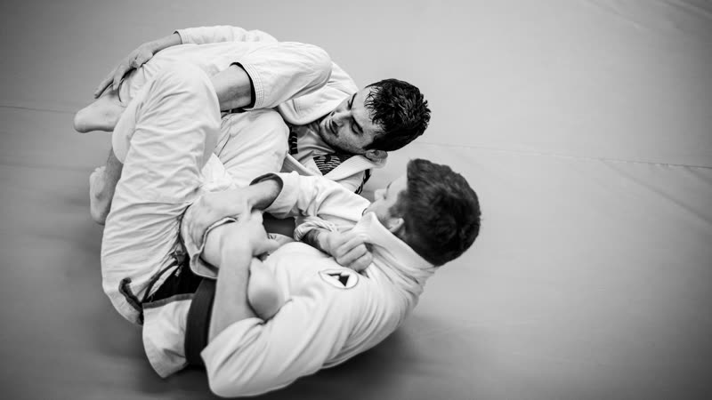 Dois lutadores de quimono treinando jiu-jítsu no chão